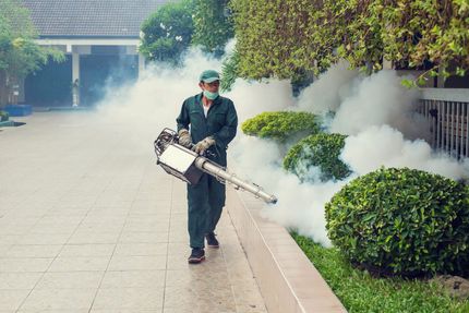 A man is using a fog machine to spray smoke on a sidewalk.