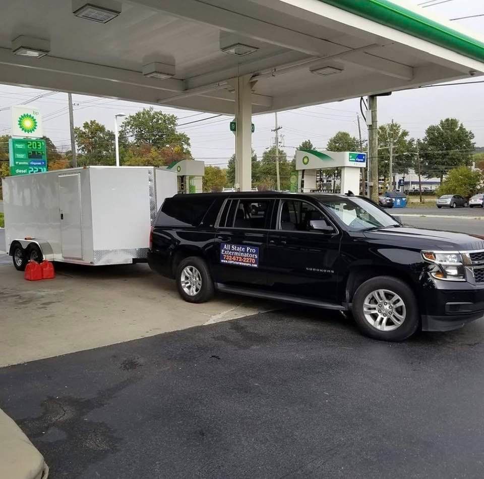 A black suv with a trailer attached to it is parked at a gas station.