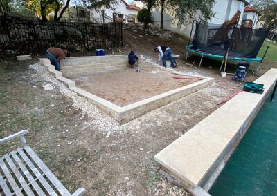 A group of people are working on a concrete patio in a backyard.