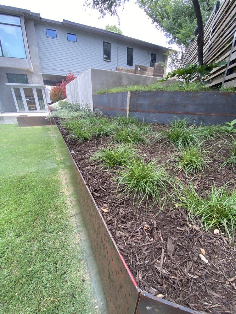 A garden with a fence and a house in the background.