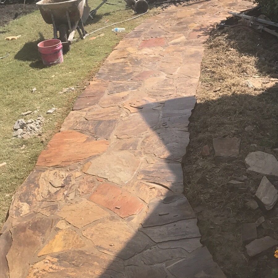 A stone walkway is being built in a yard next to a wheelbarrow.
