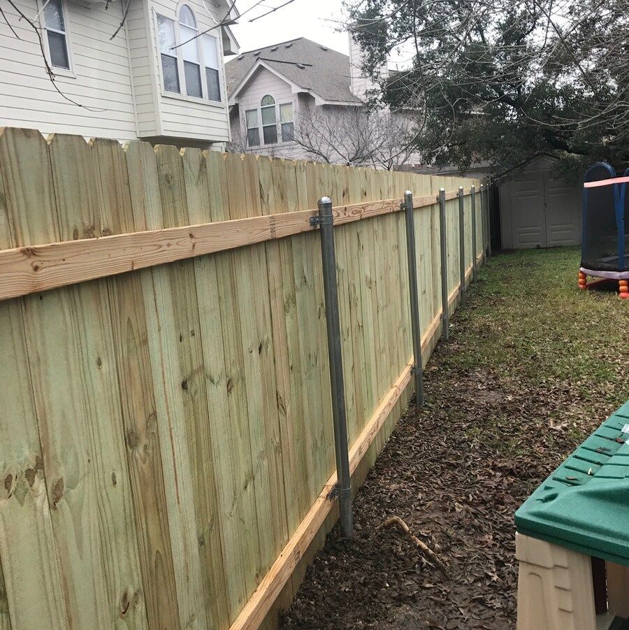 A wooden fence in a backyard with a trampoline in the background.