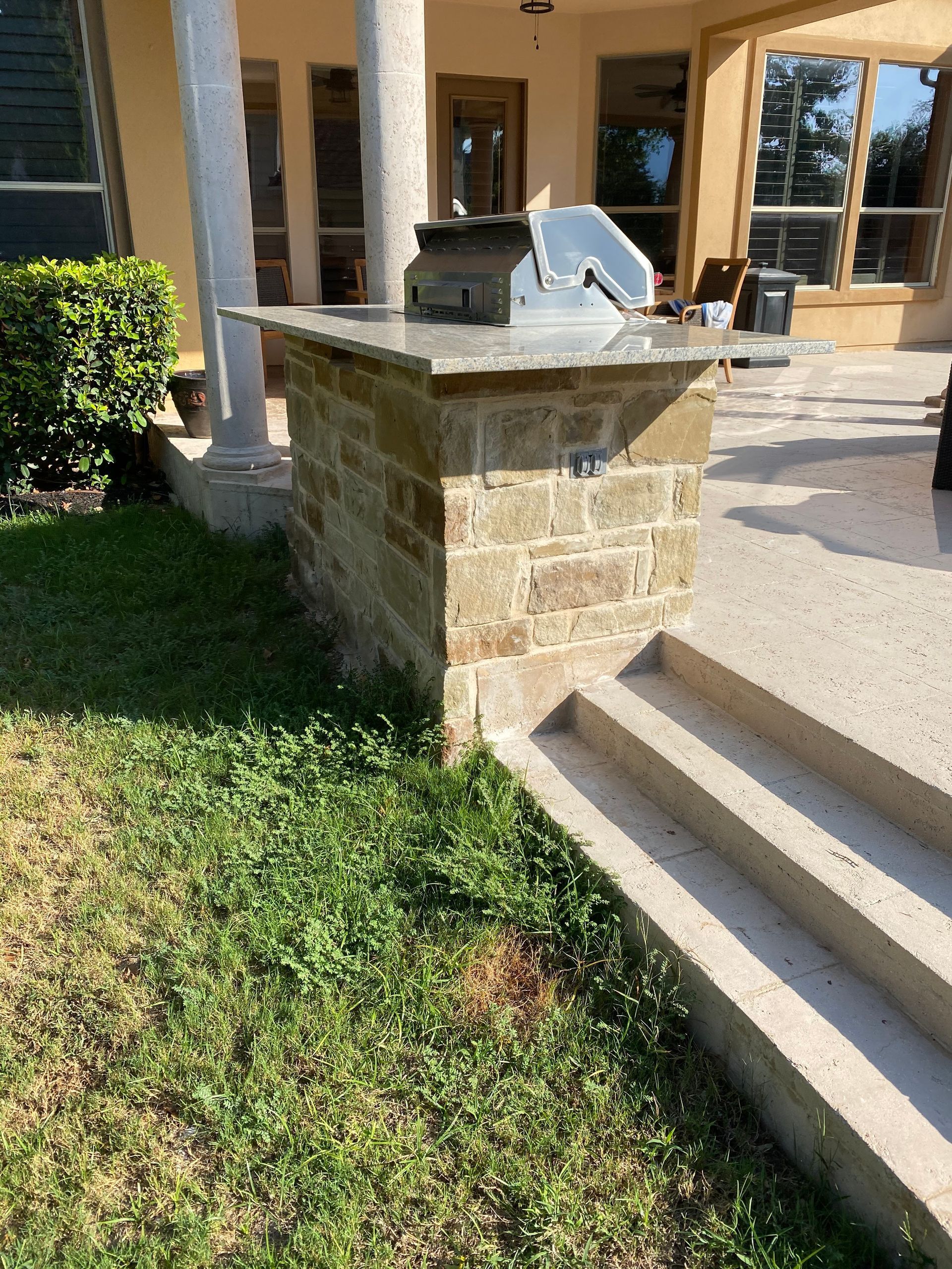 A brick pillar with a grill on top of it in front of a house.