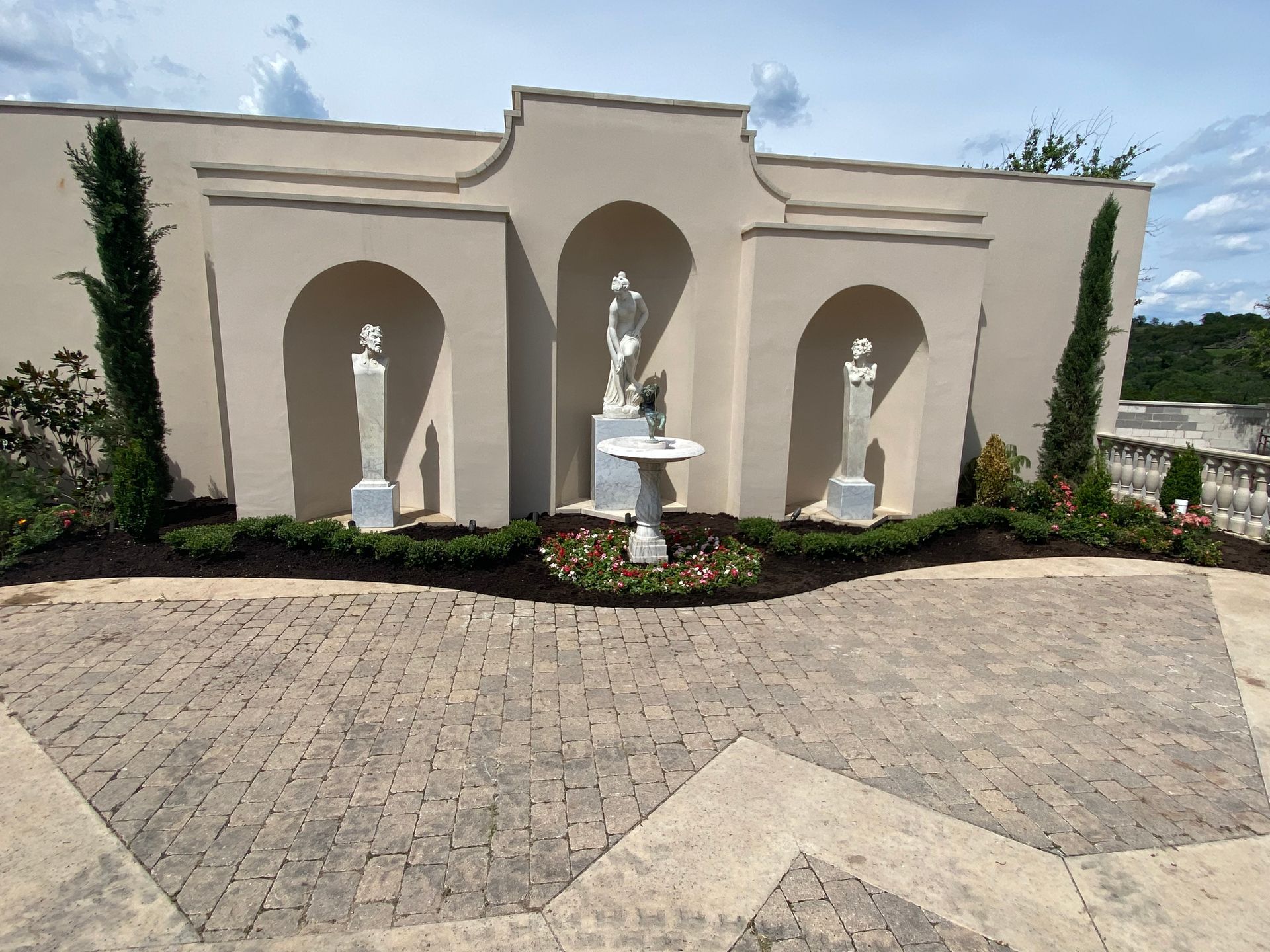 A statue of a woman is in front of a wall with arches and a fountain.
