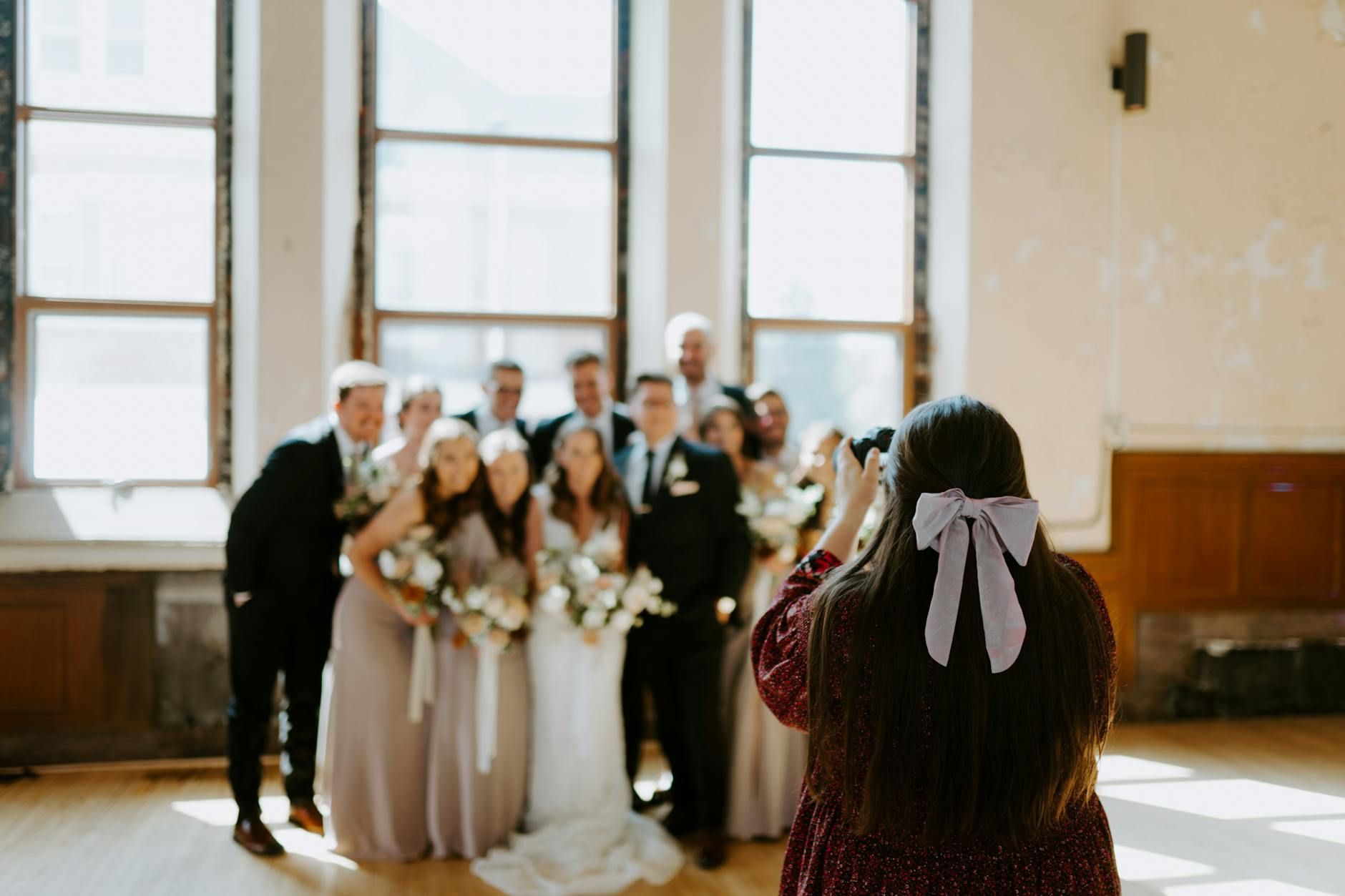 A photographer capturing a wedding party in a sunlit indoor hall venue in Corsicana, Texas.