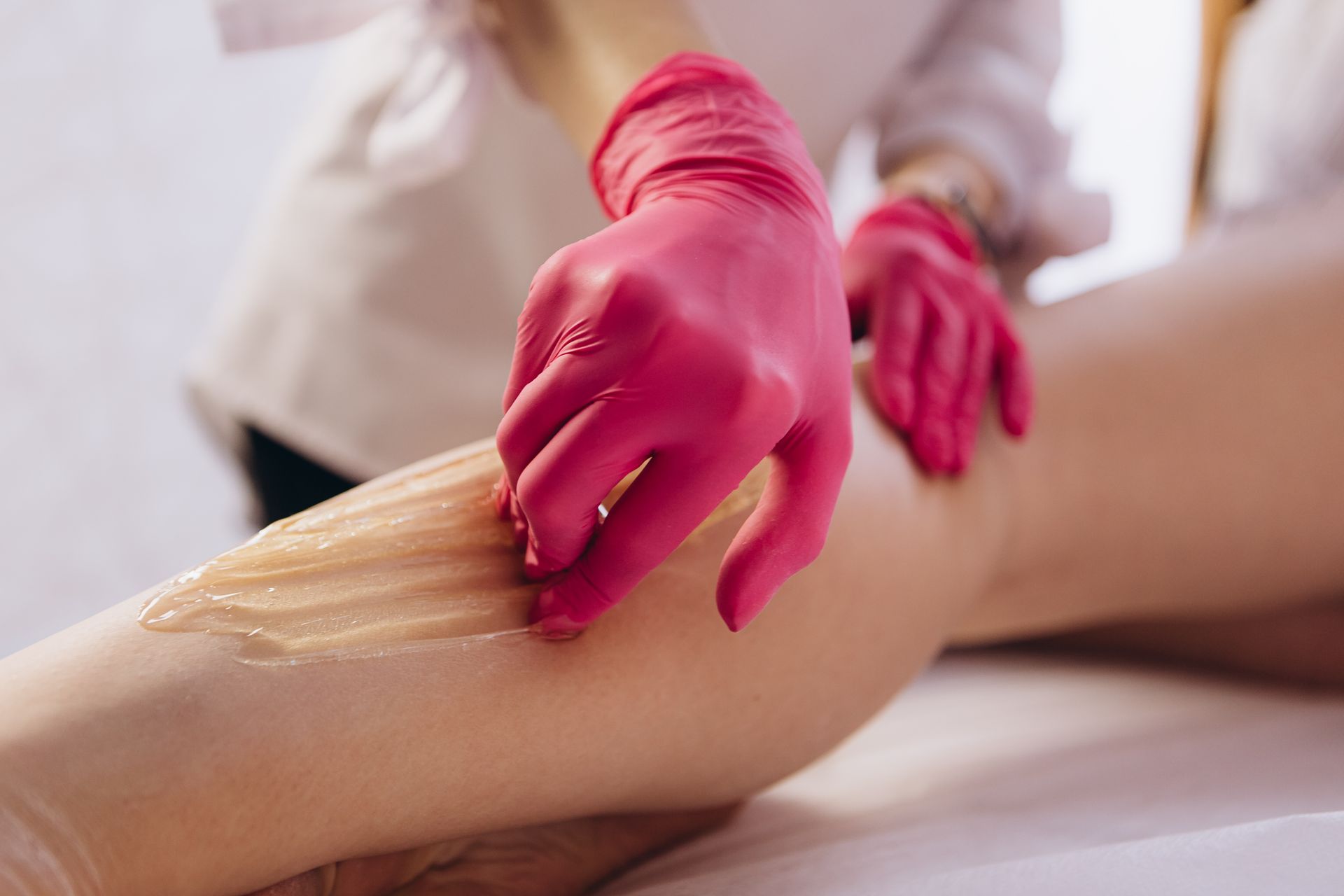 Person in pink gloves applying wax to leg for hair removal