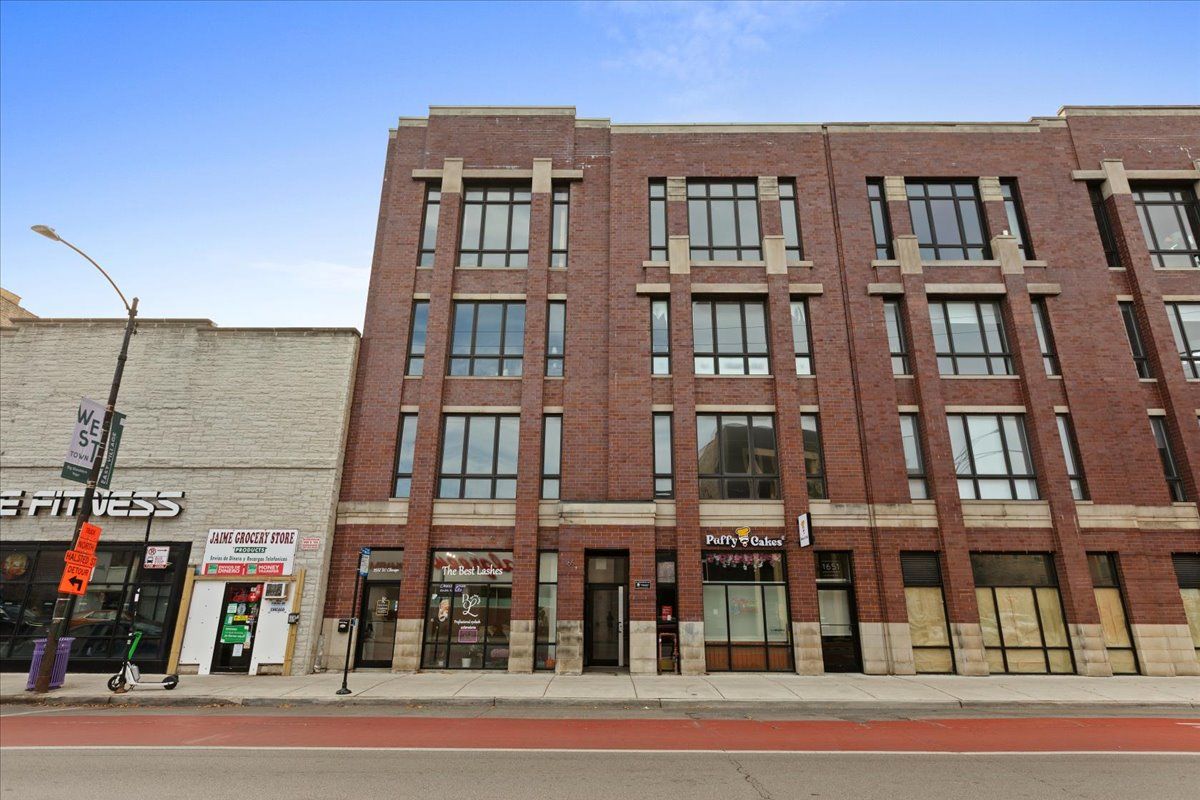 Brick building with retail storefronts, red road, and light blue sky.