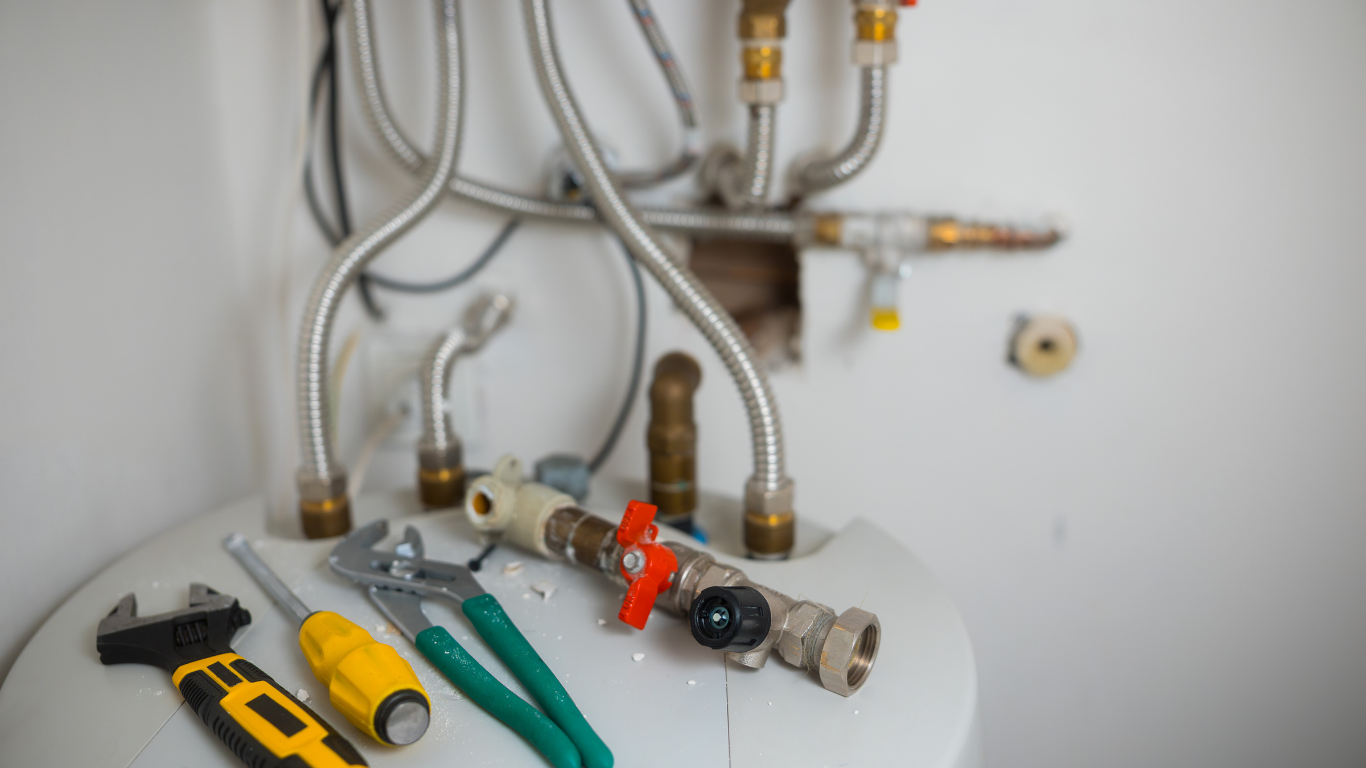 Plumbing tools on top of a water heater with pipes and connections.