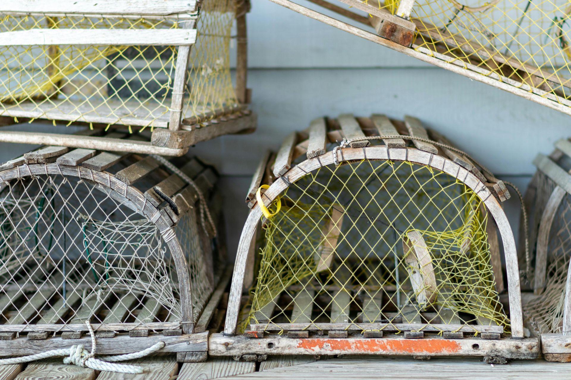 Wooden lobster traps with yellow netting stacked against a blue wall.