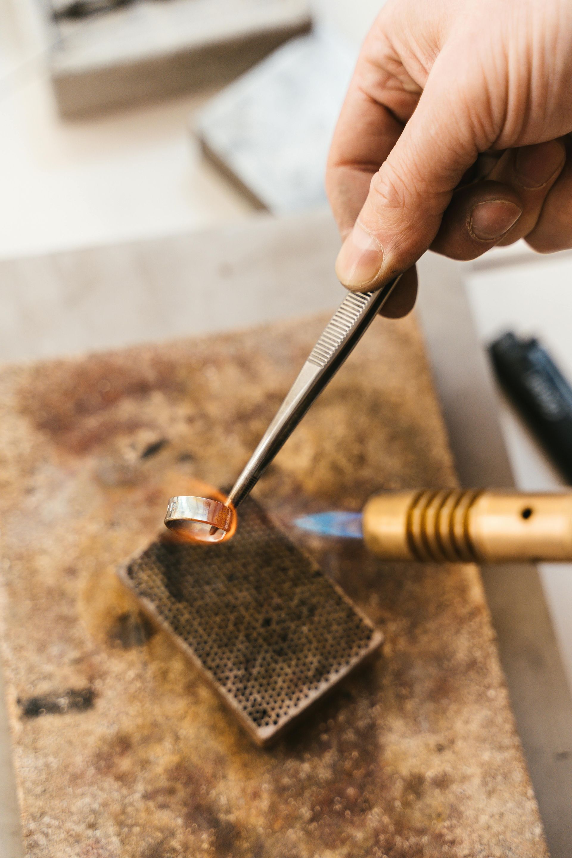 A person soldering a ring with a torch and tweezers on a brick.