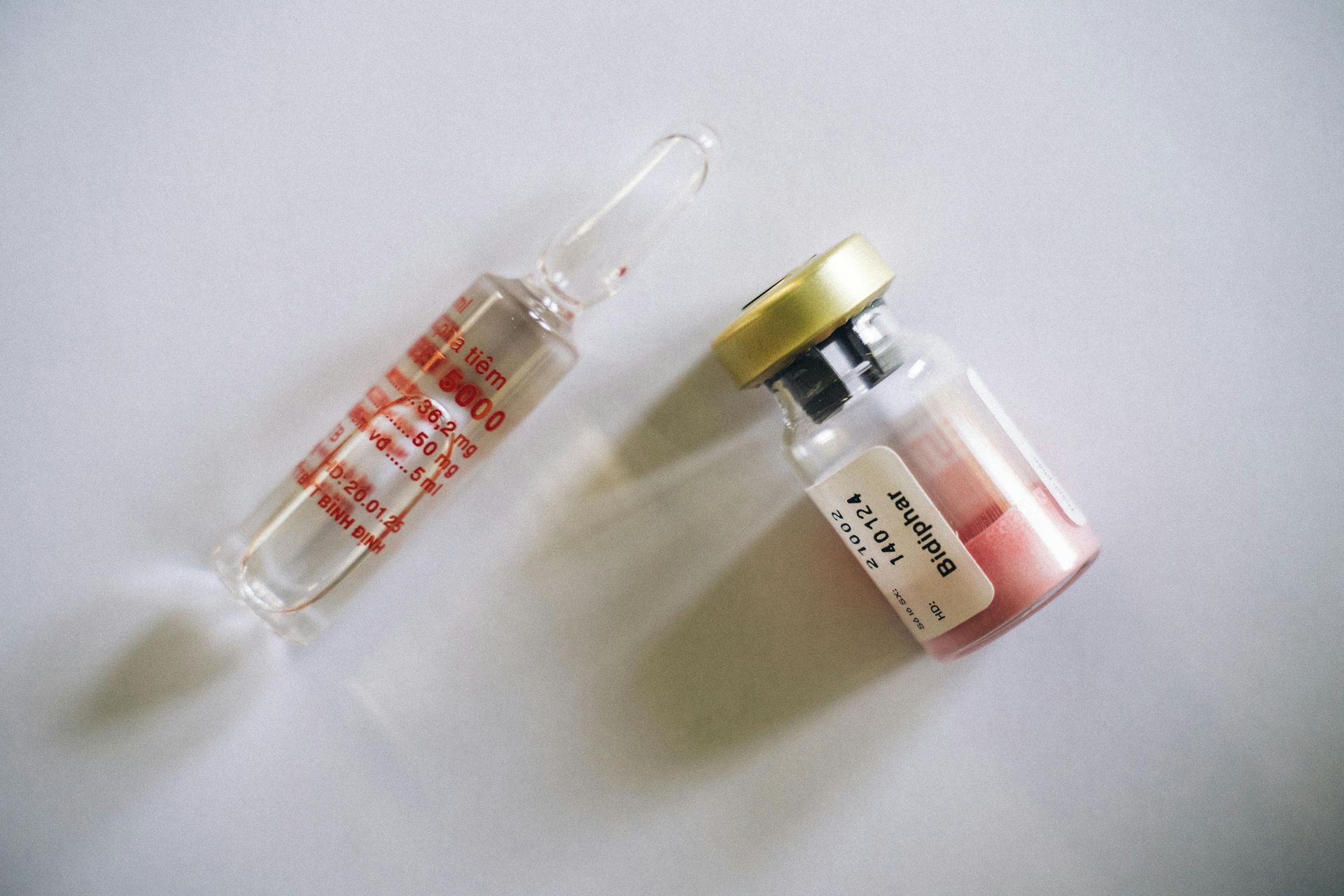 Two medicine vials: one glass ampule, the other a pink powder filled bottle.