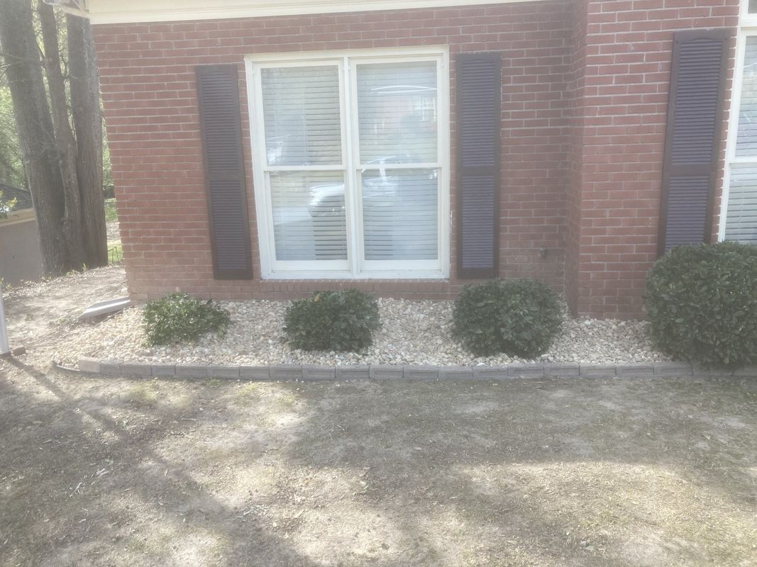 A brick house with a window and bushes in front of it.