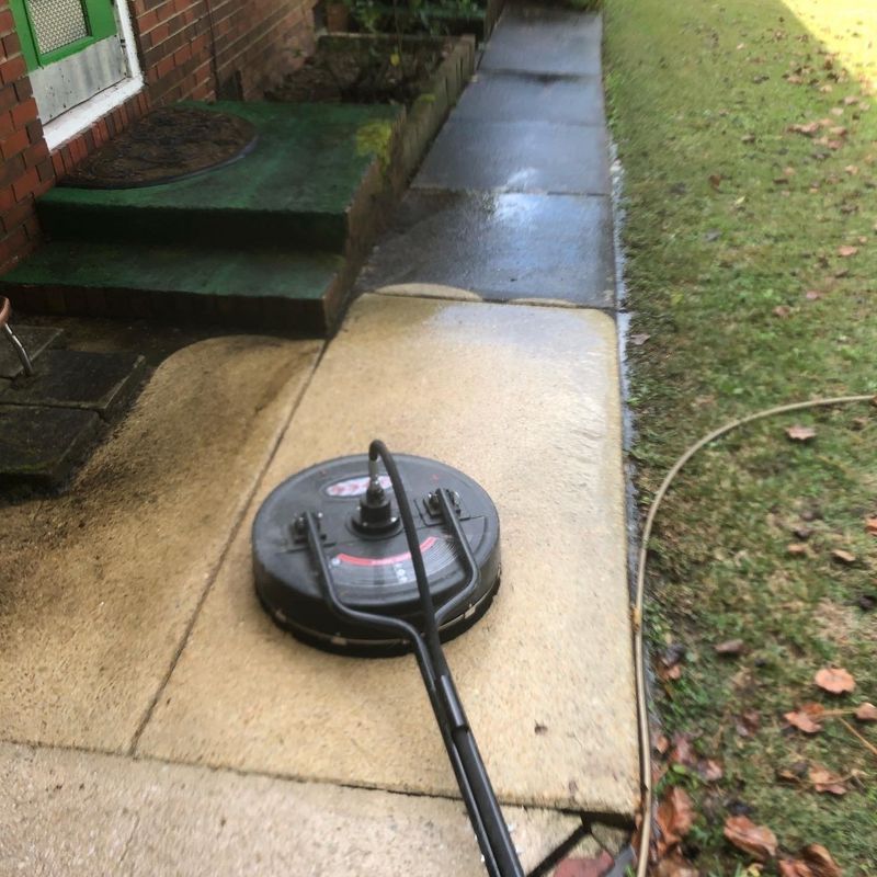 A pressure washer is being used to clean a sidewalk in front of a house.