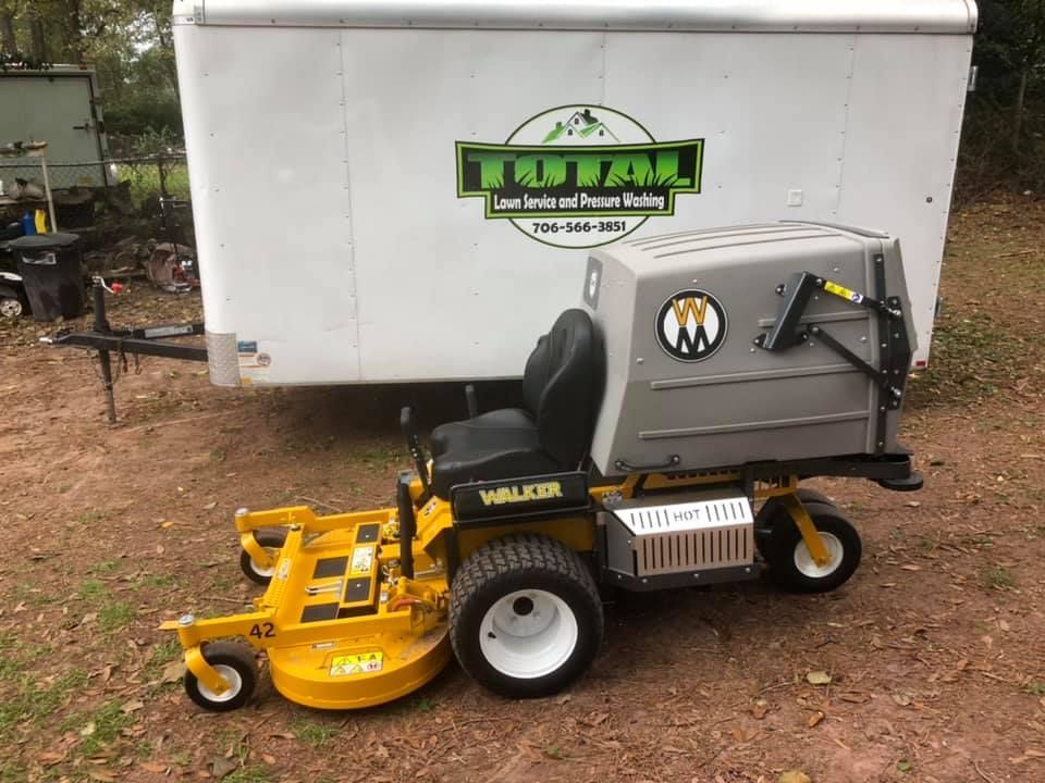 A yellow lawn mower is parked in front of a trailer.