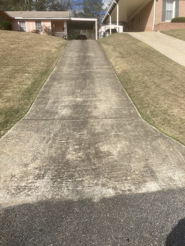 A dirty concrete driveway leading to a house.