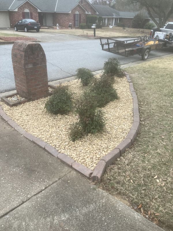 A lawn mower is parked on the side of the road next to a garden.