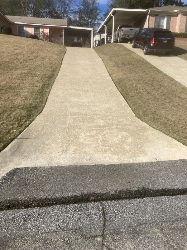 A concrete driveway leading to a house with a car parked under a carport.