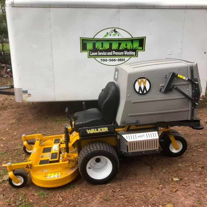 Yellow Walker lawn mower with a gray collection box in front of a white trailer.