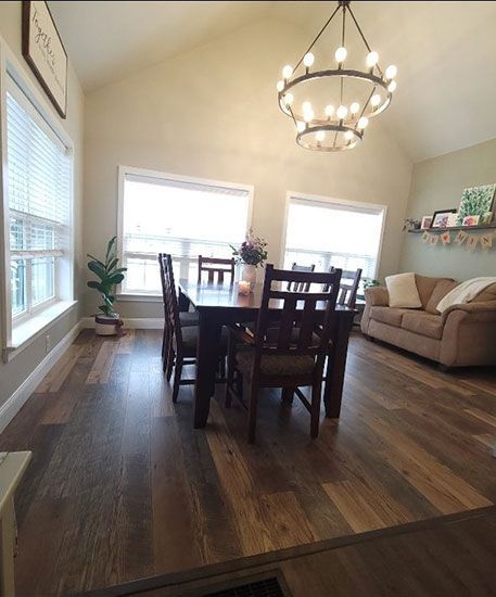 Dining room with dark wood table, chairs, tan sofa, hardwood floor, and chandelier.