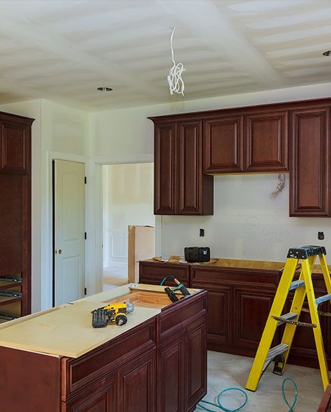 Kitchen remodel in progress: brown cabinets, island, yellow ladder, and exposed wiring.