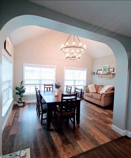 Dining room with a long table, chairs, and a chandelier. There's a couch and windows.