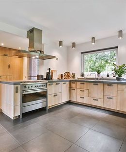 Modern kitchen with light wood cabinets, stainless steel appliances, and dark gray tile floor.