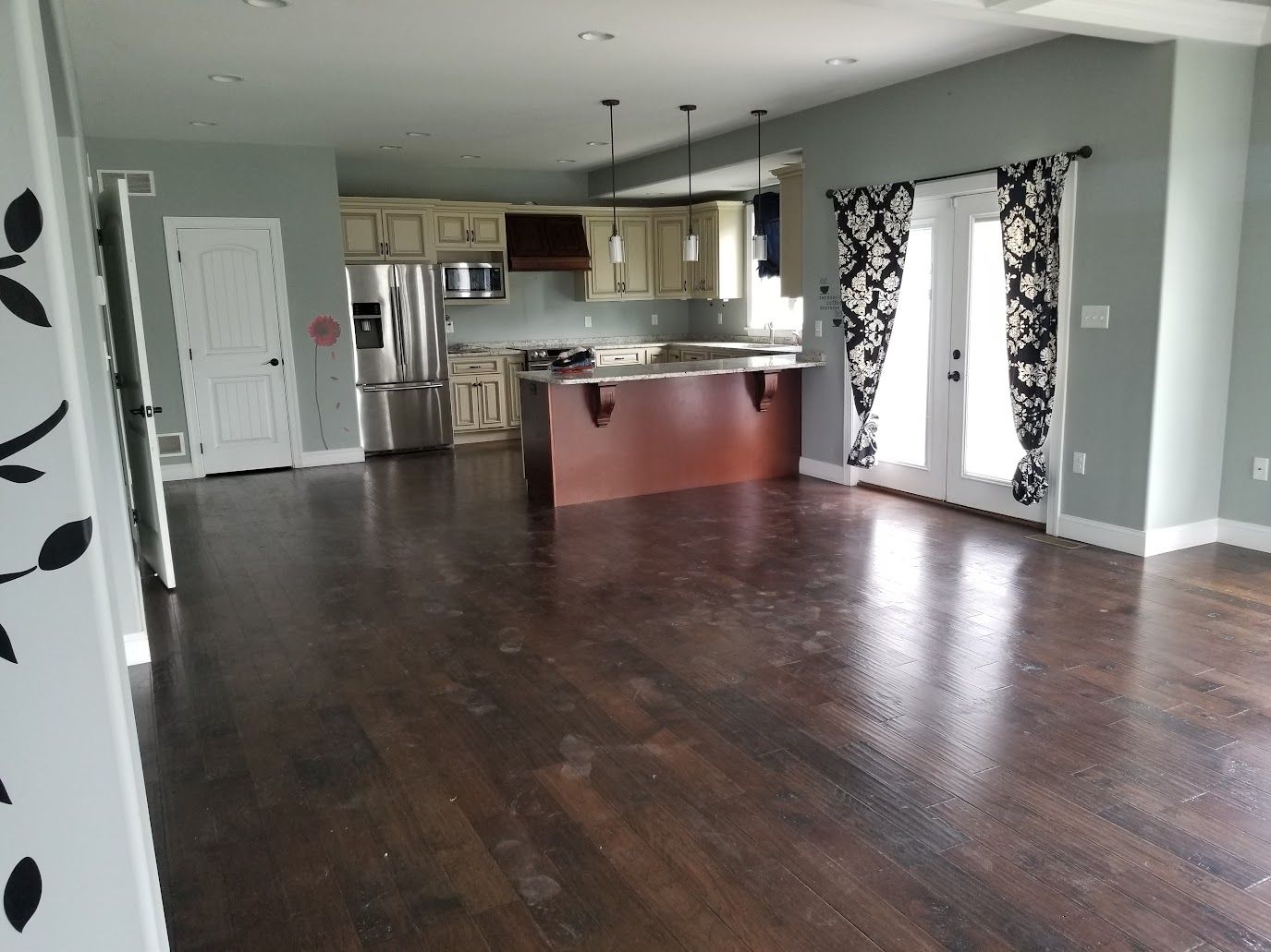 Open-concept kitchen and living space with dark wood floors, pale blue walls, and cream-colored cabinets.