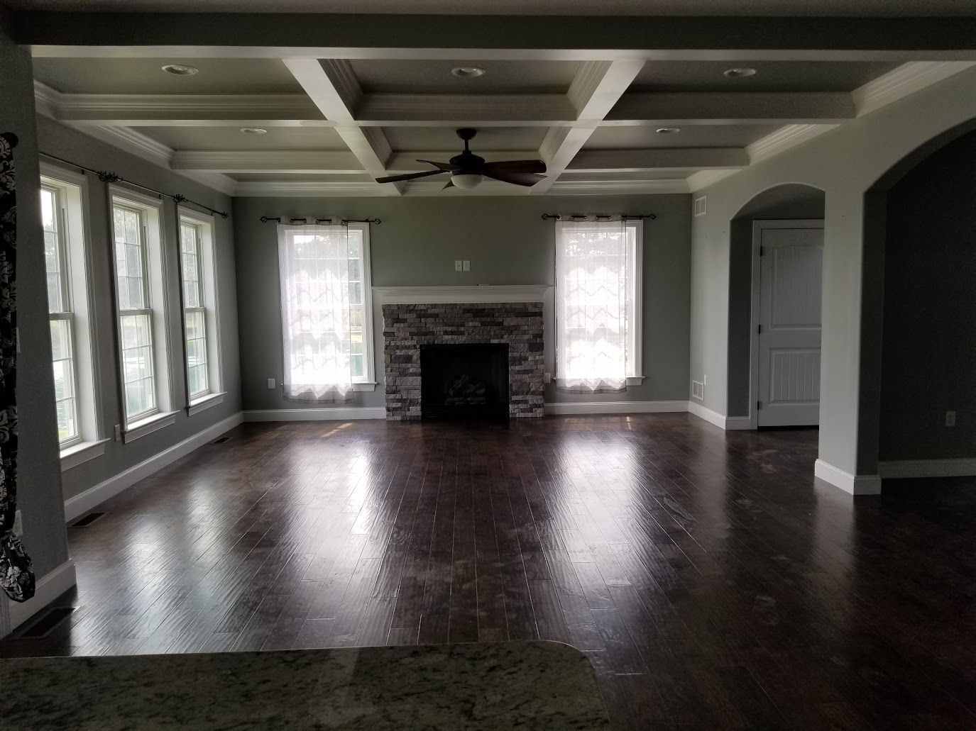 Empty living room with a fireplace, dark hardwood floors, and a coffered ceiling.