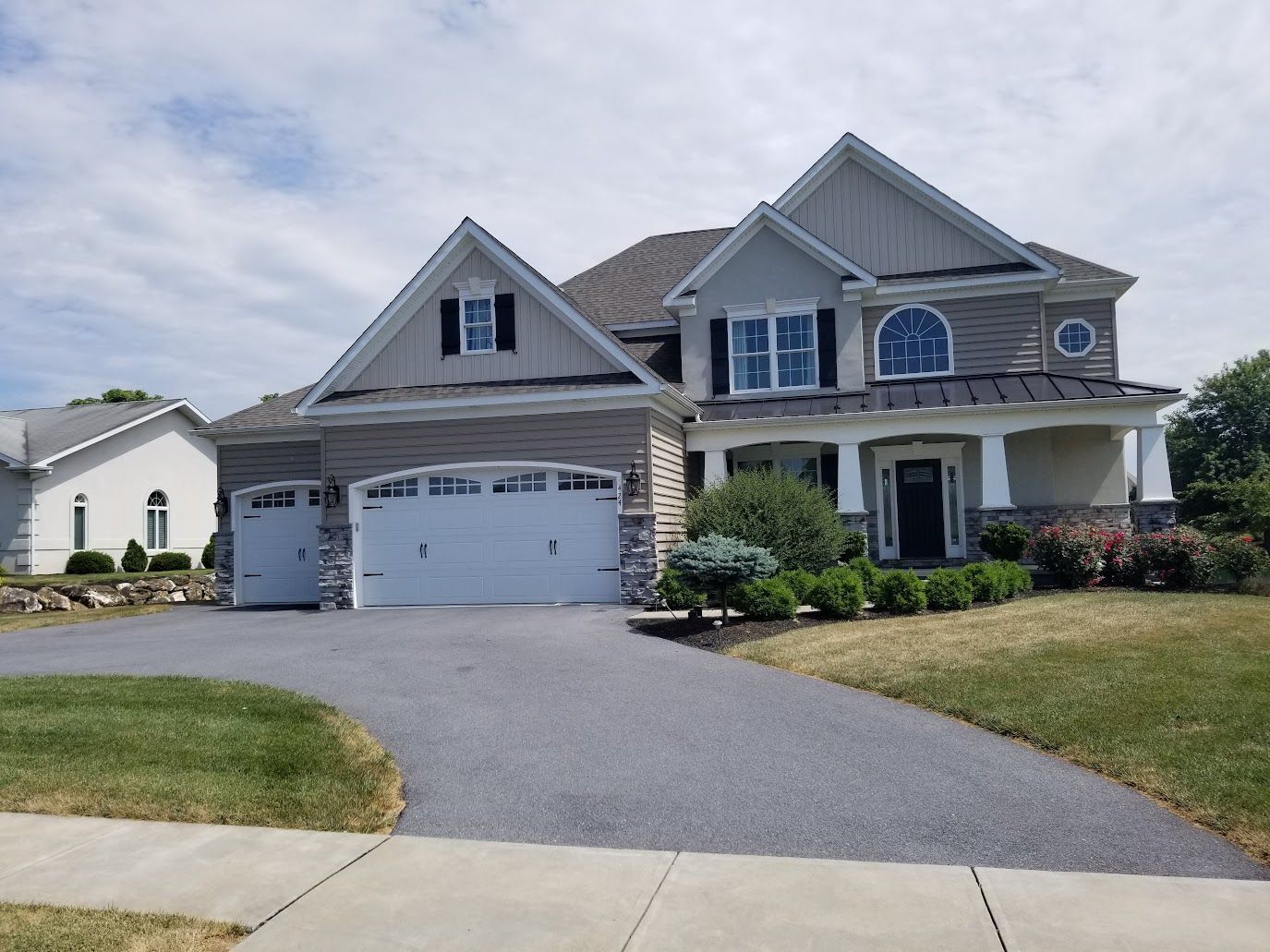Two-story house with a gray driveway and garage. The exterior has a combination of stone, siding, and gray roof.