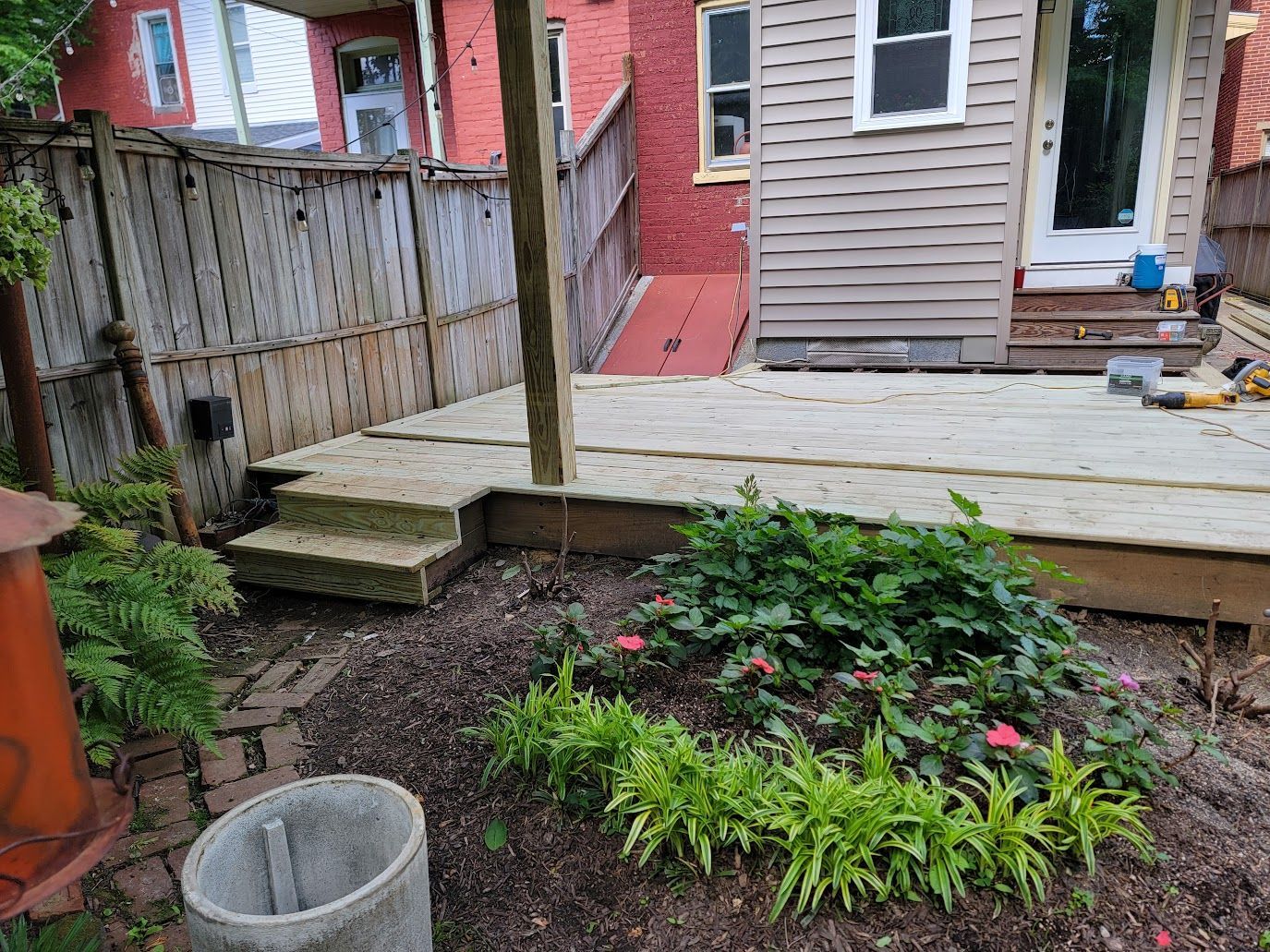 Backyard with a wooden deck, stairs, garden with flowers, and a wooden fence.