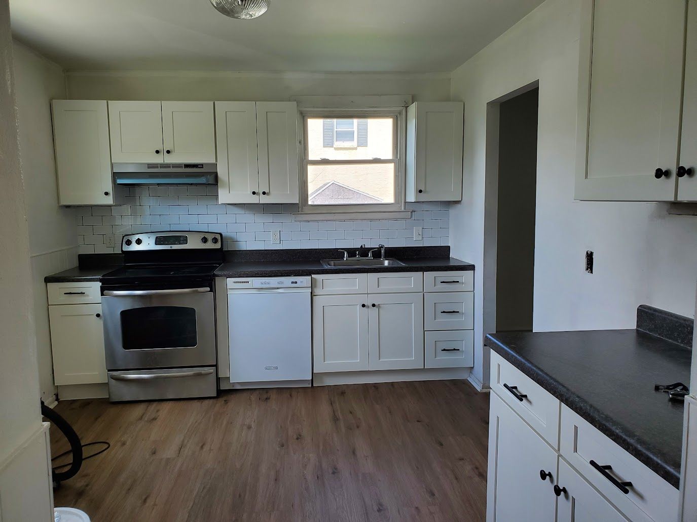 White kitchen with stainless steel appliances, white cabinets, and dark countertops.