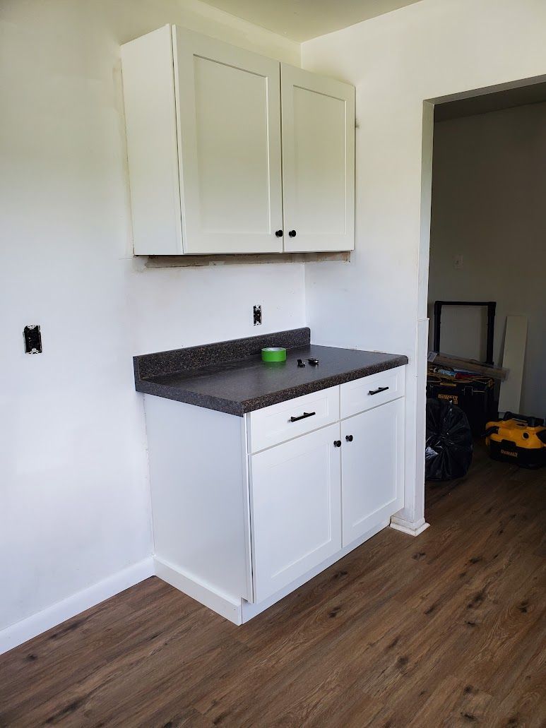 White kitchen cabinets, dark countertop, hardwood floor.