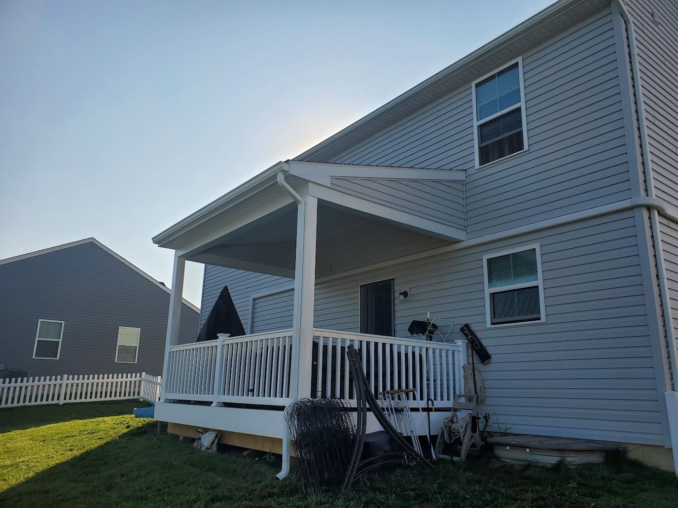 A two-story house with a covered deck, white railings, and light blue siding, on a sunny day.