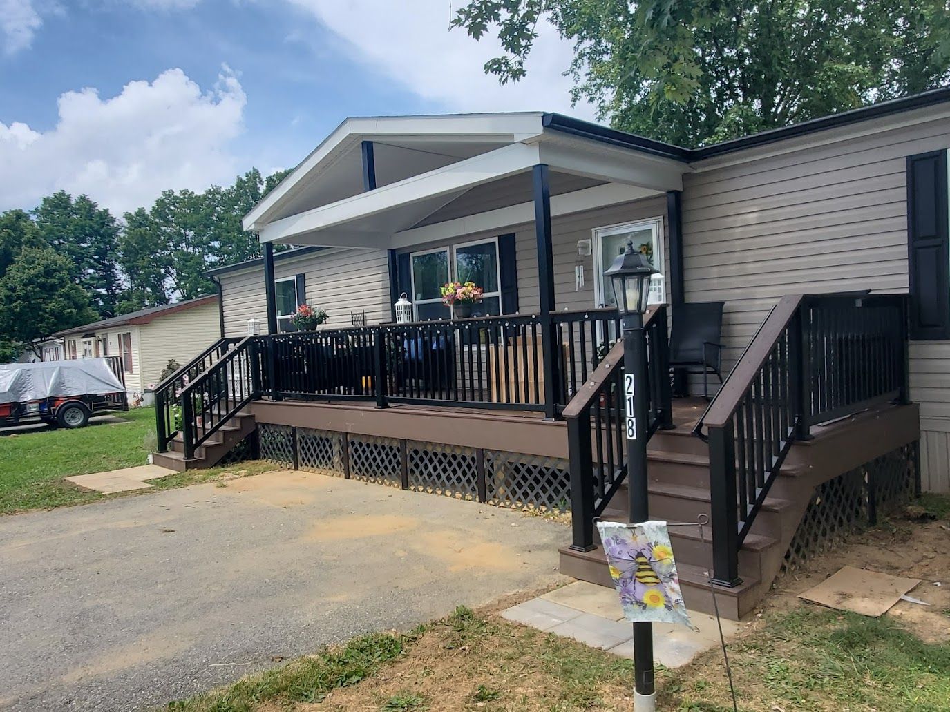 Mobile home with a porch, brown deck, black railing, and beige siding.