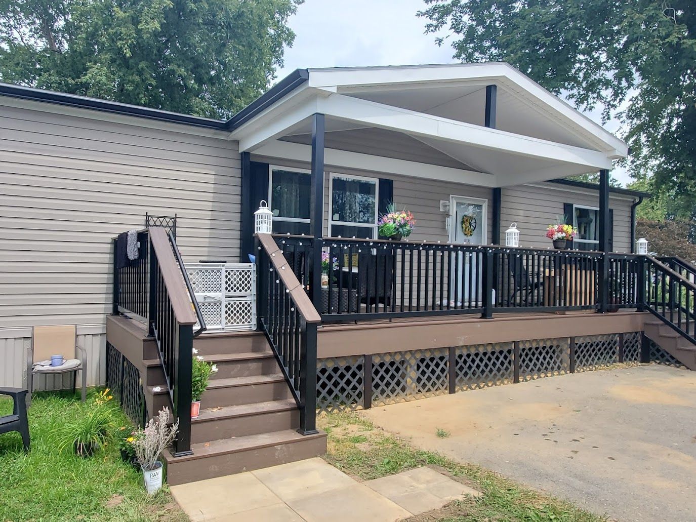 Mobile home with porch, brown deck, steps, beige siding, and flowerpots.
