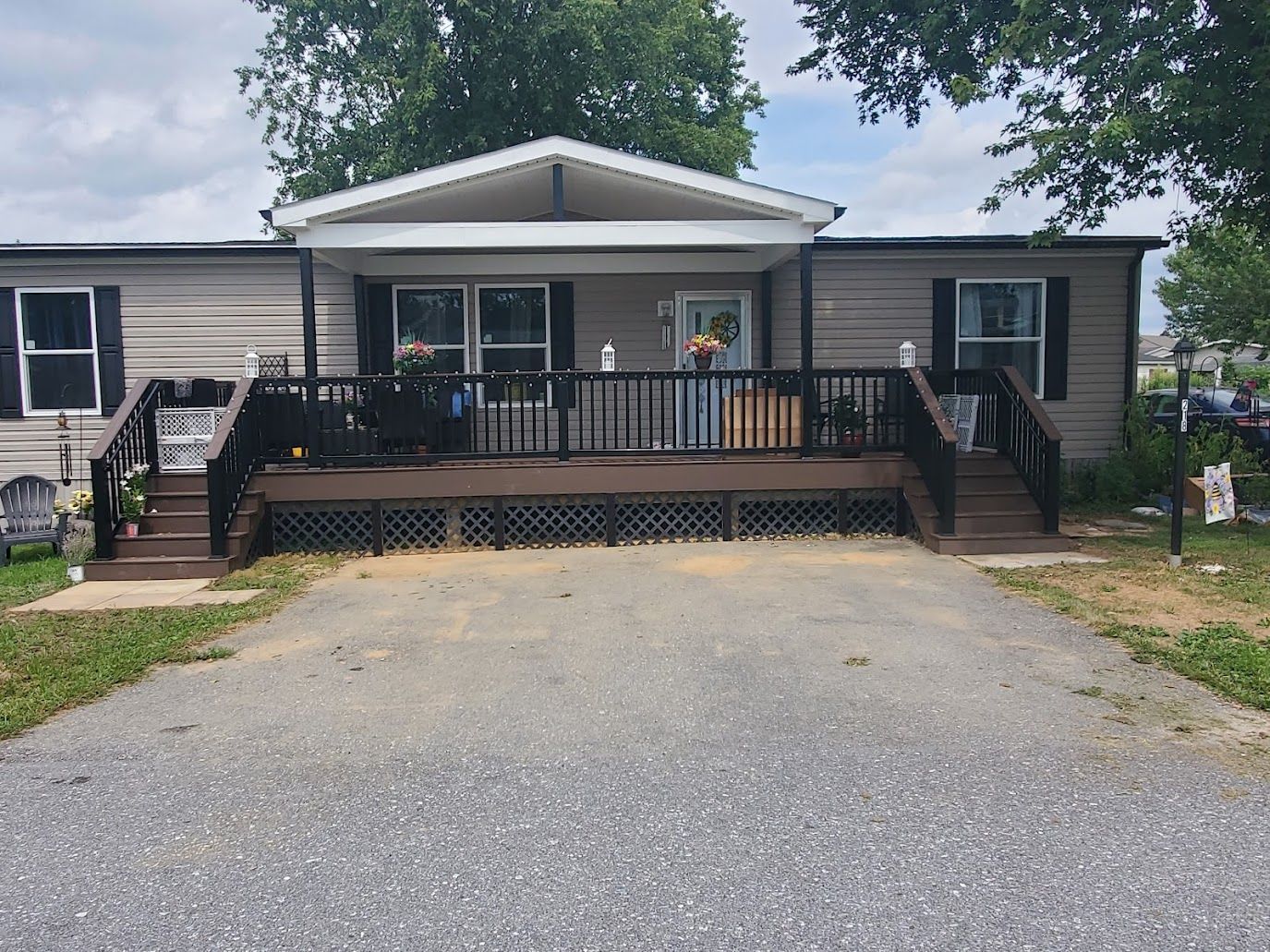 Mobile home with a porch and dark brown deck, gray siding, and gravel driveway.