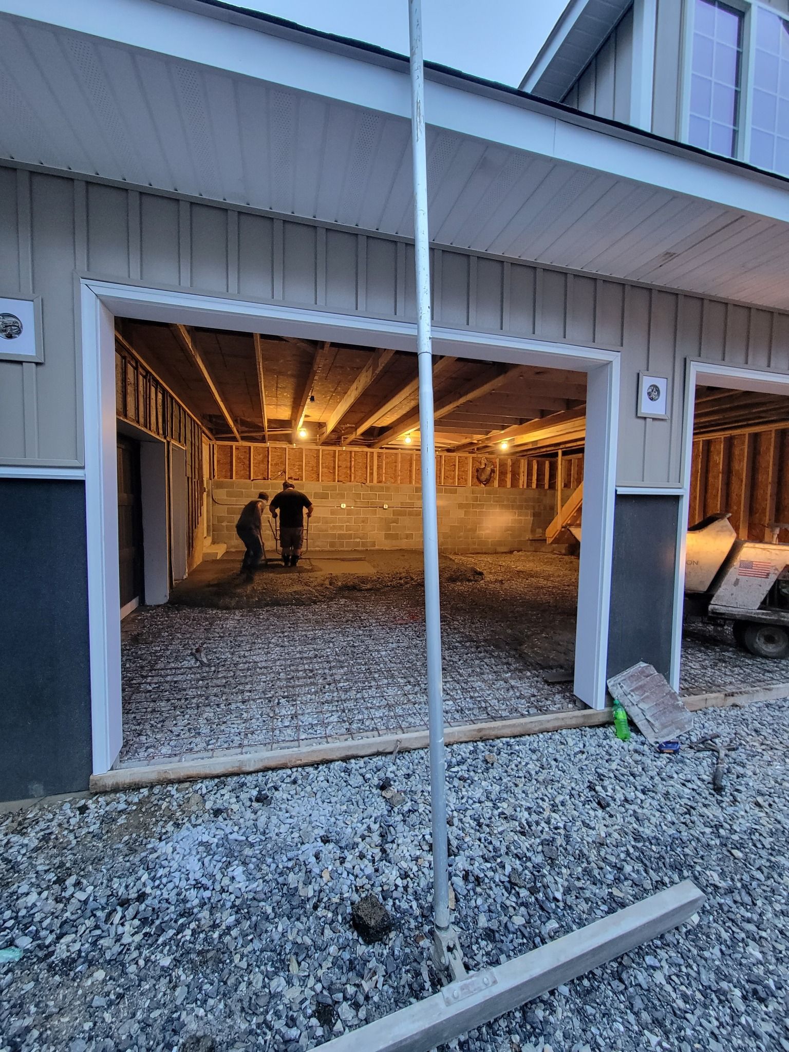 Garage under construction, showing framing, concrete floor, and workers inside.