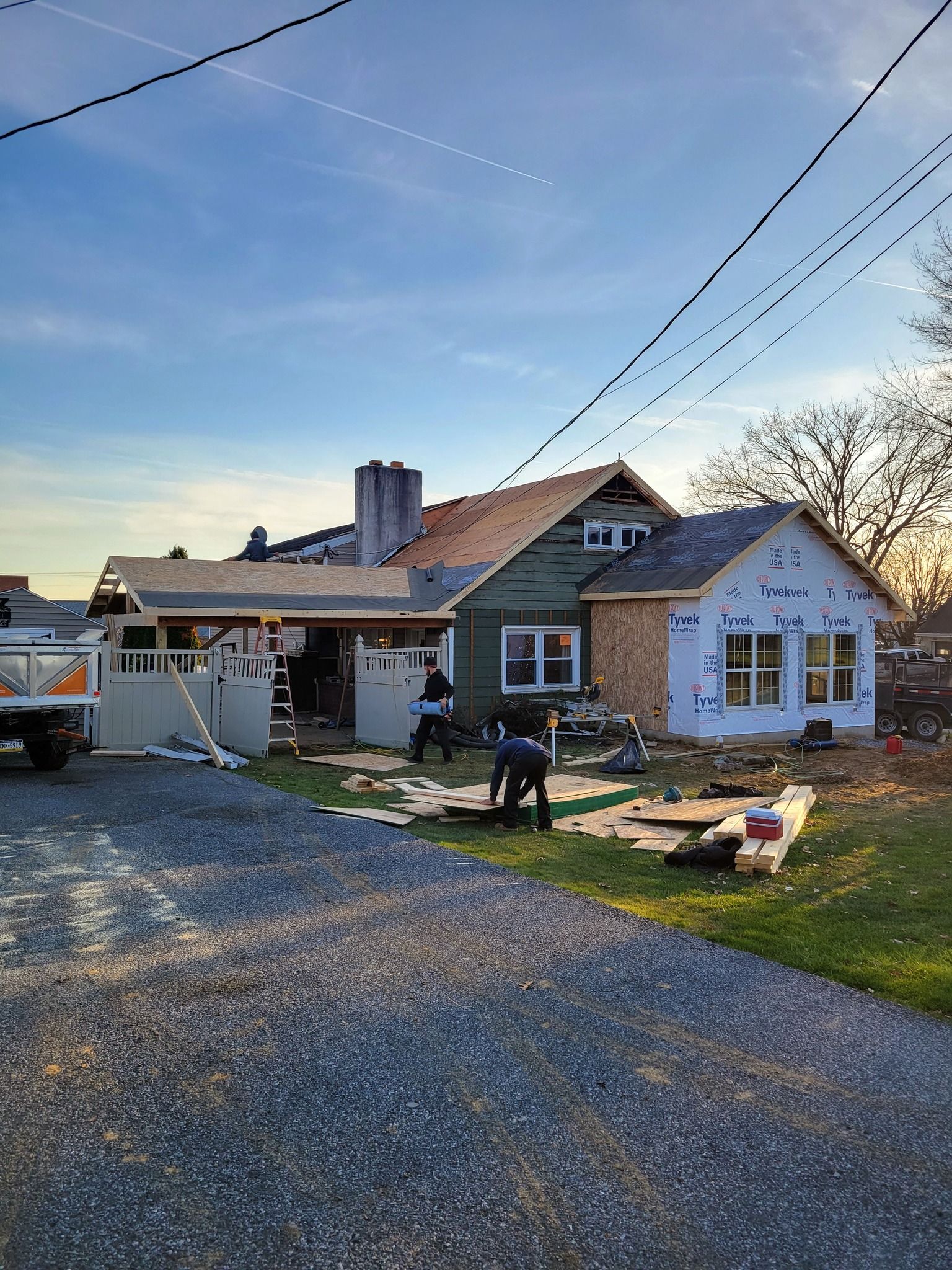 House under construction; workers on site; new siding, blue wrap, and wood accents.