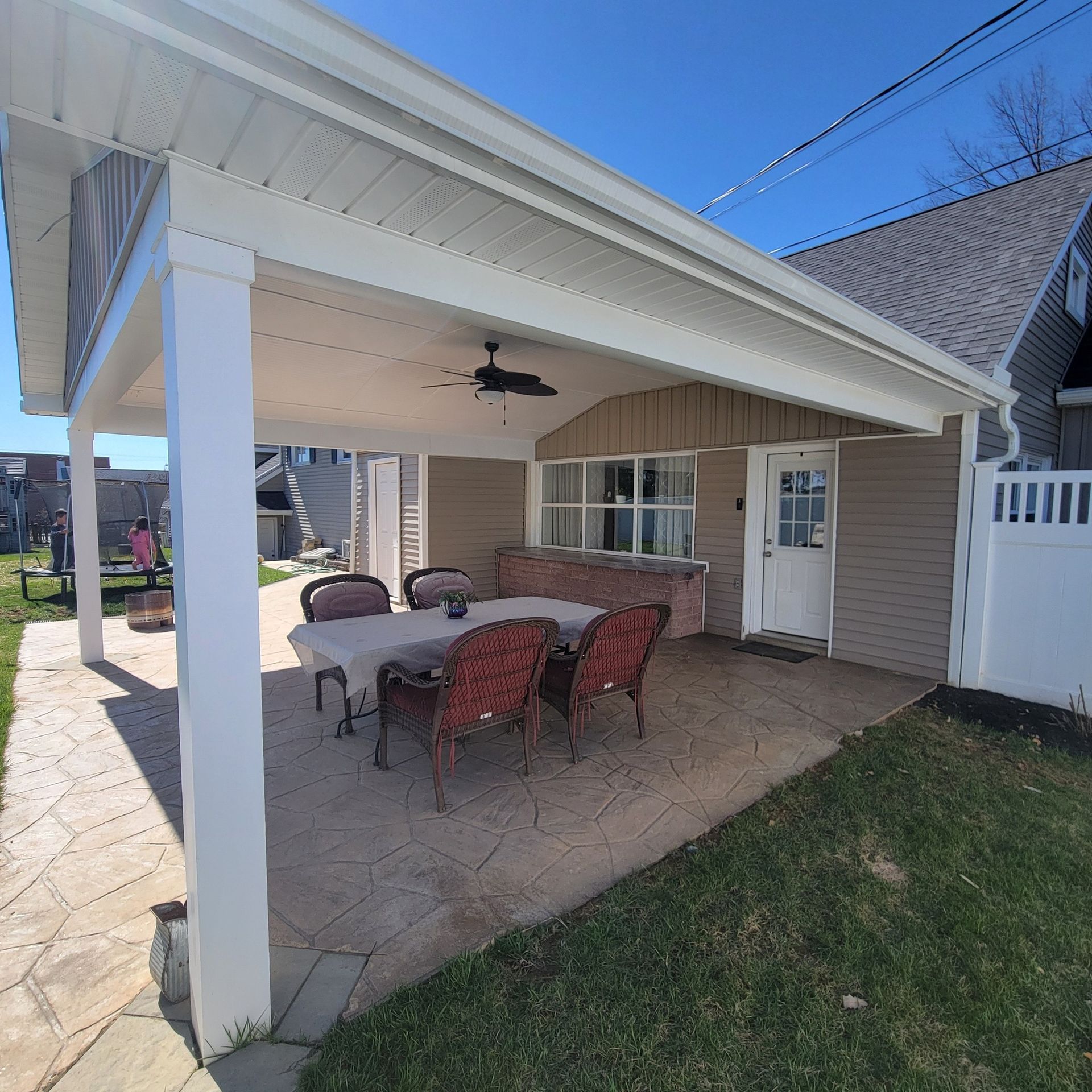 Patio with dining set under a white roof, next to a tan house with a white door.
