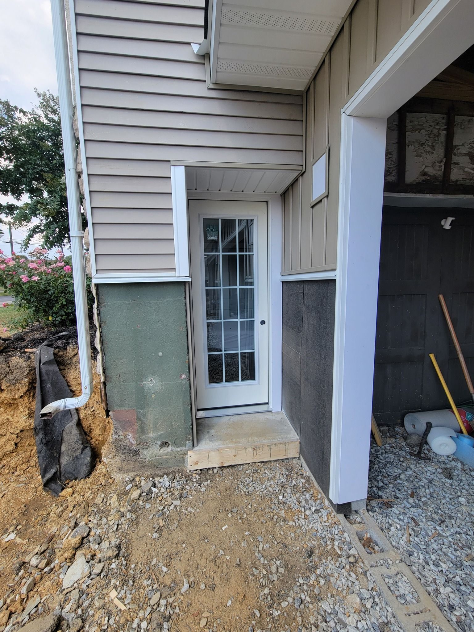 A doorway to a house, partially underground with exposed soil, and a garage to the right.