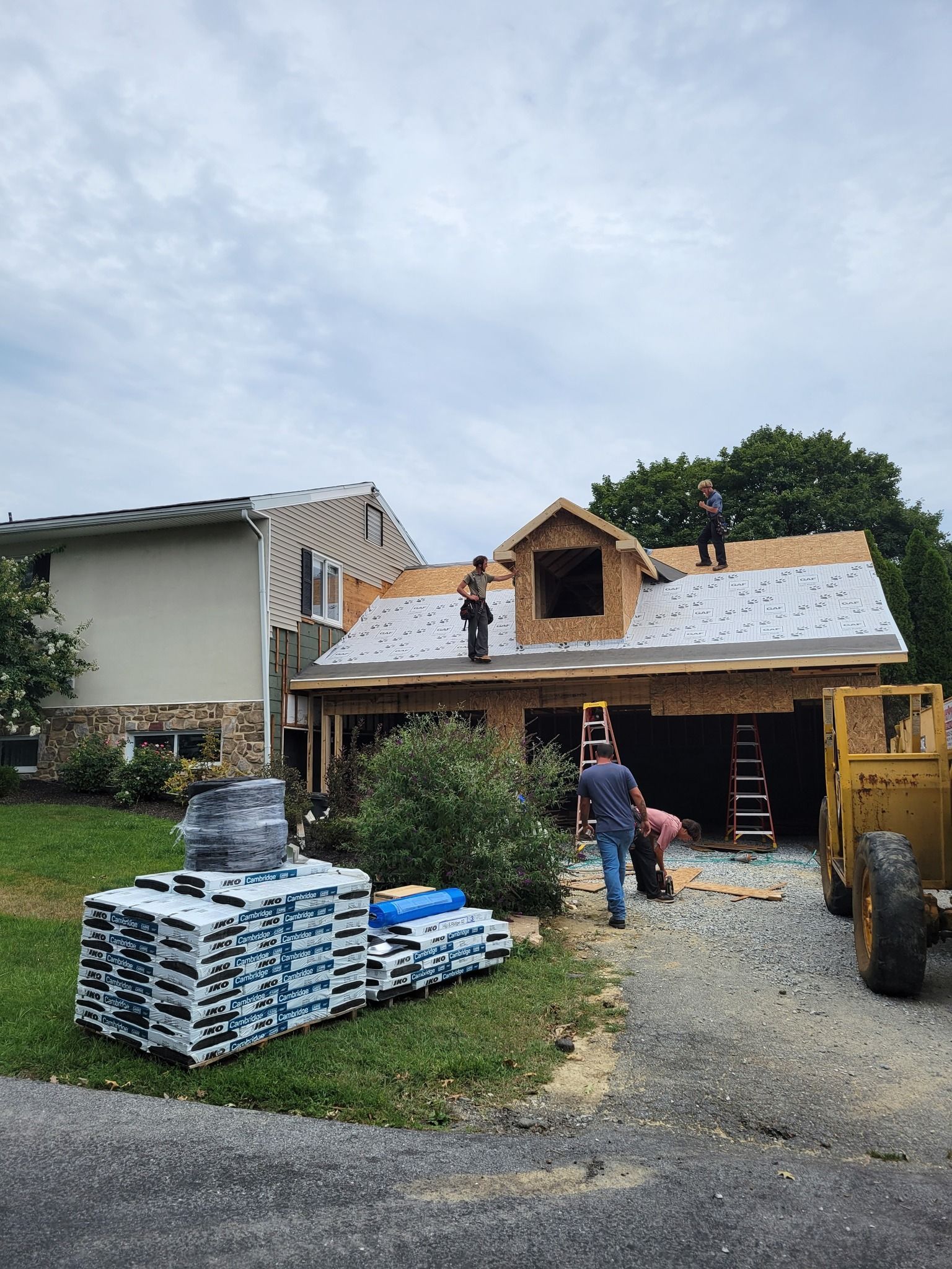 Roofers working on a house under construction; materials and equipment on the ground.