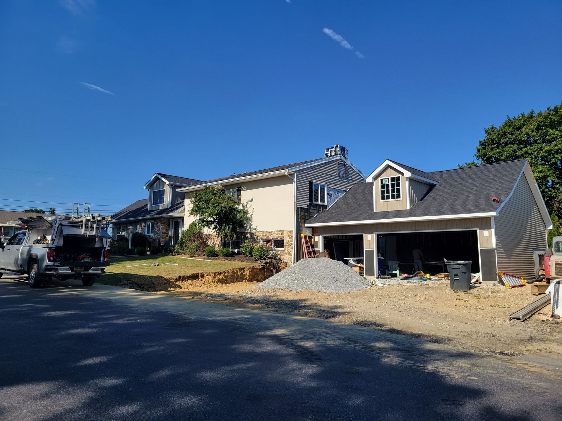 Construction site with two-story house, garage, and debris. Bright blue sky.