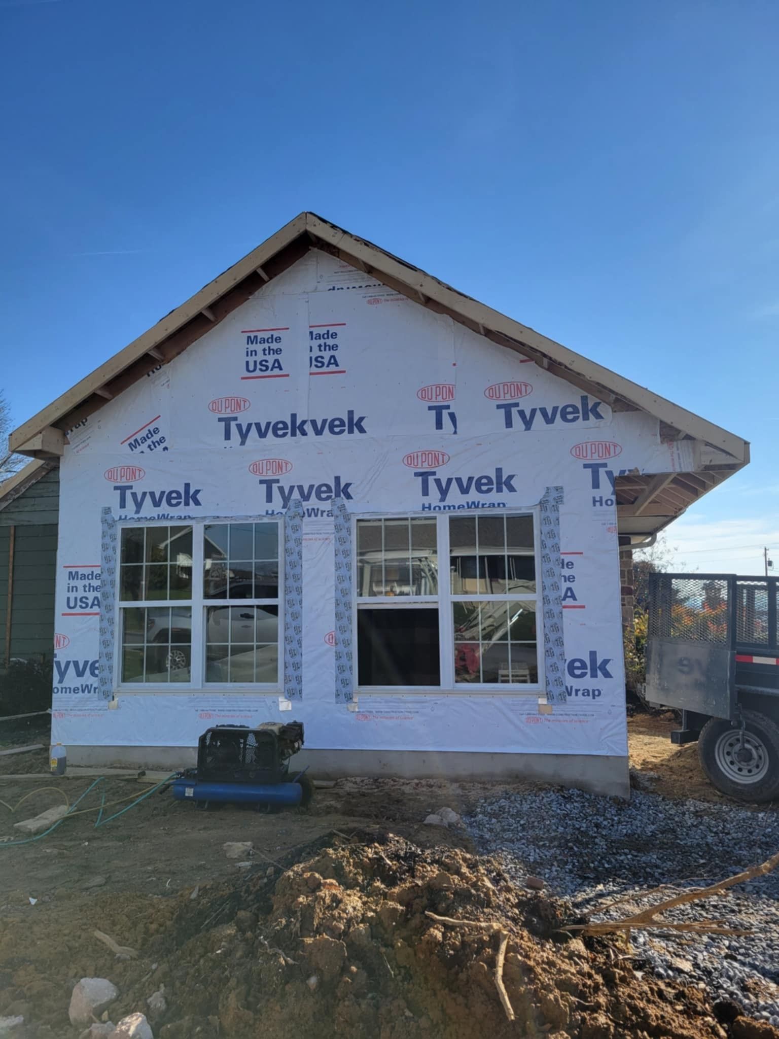 House under construction, Tyvek wrap on walls, windows installed, against a blue sky.