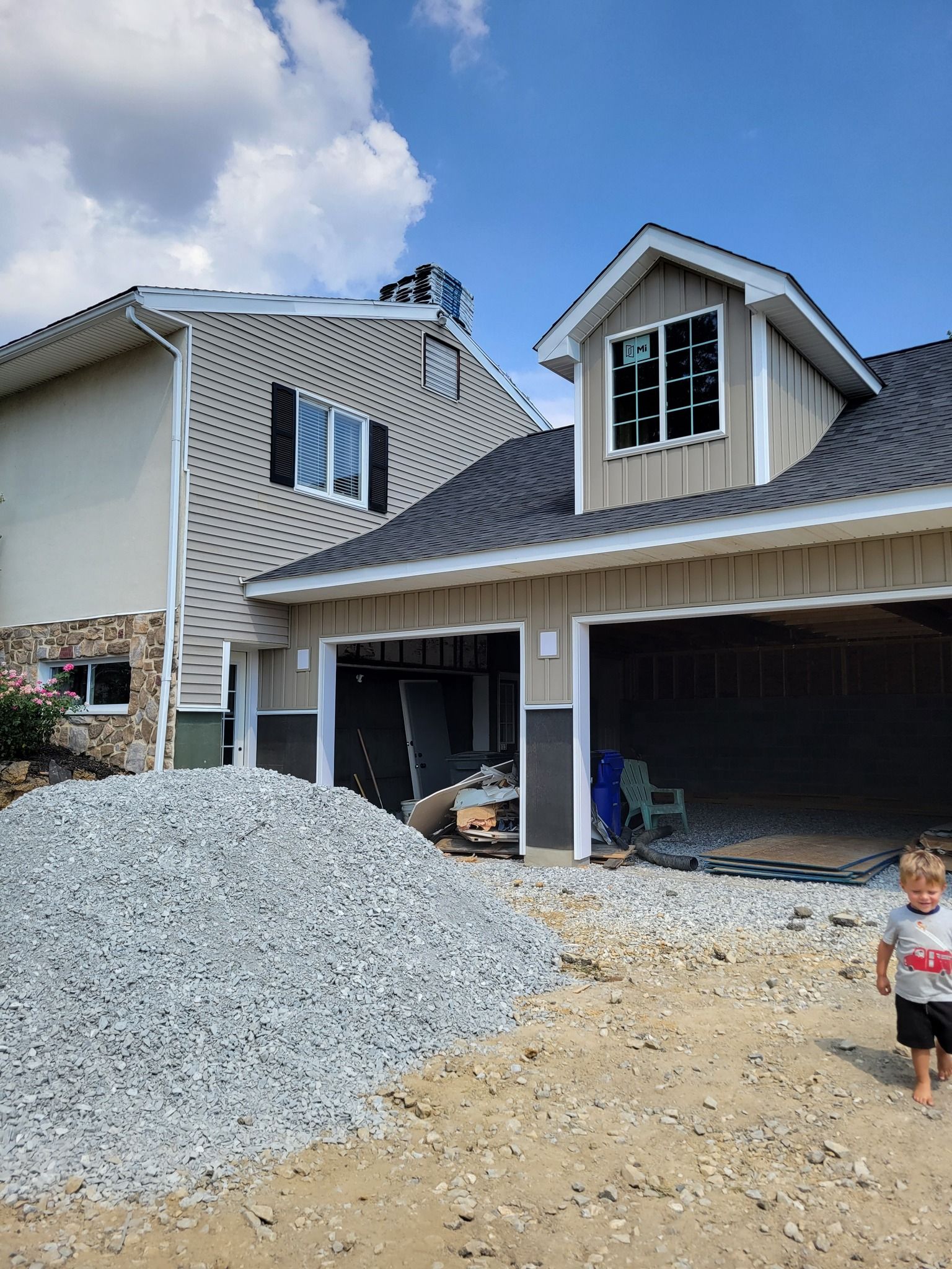 Construction site with a pile of gravel, two-car garage, child walking, and partially built house with light siding.