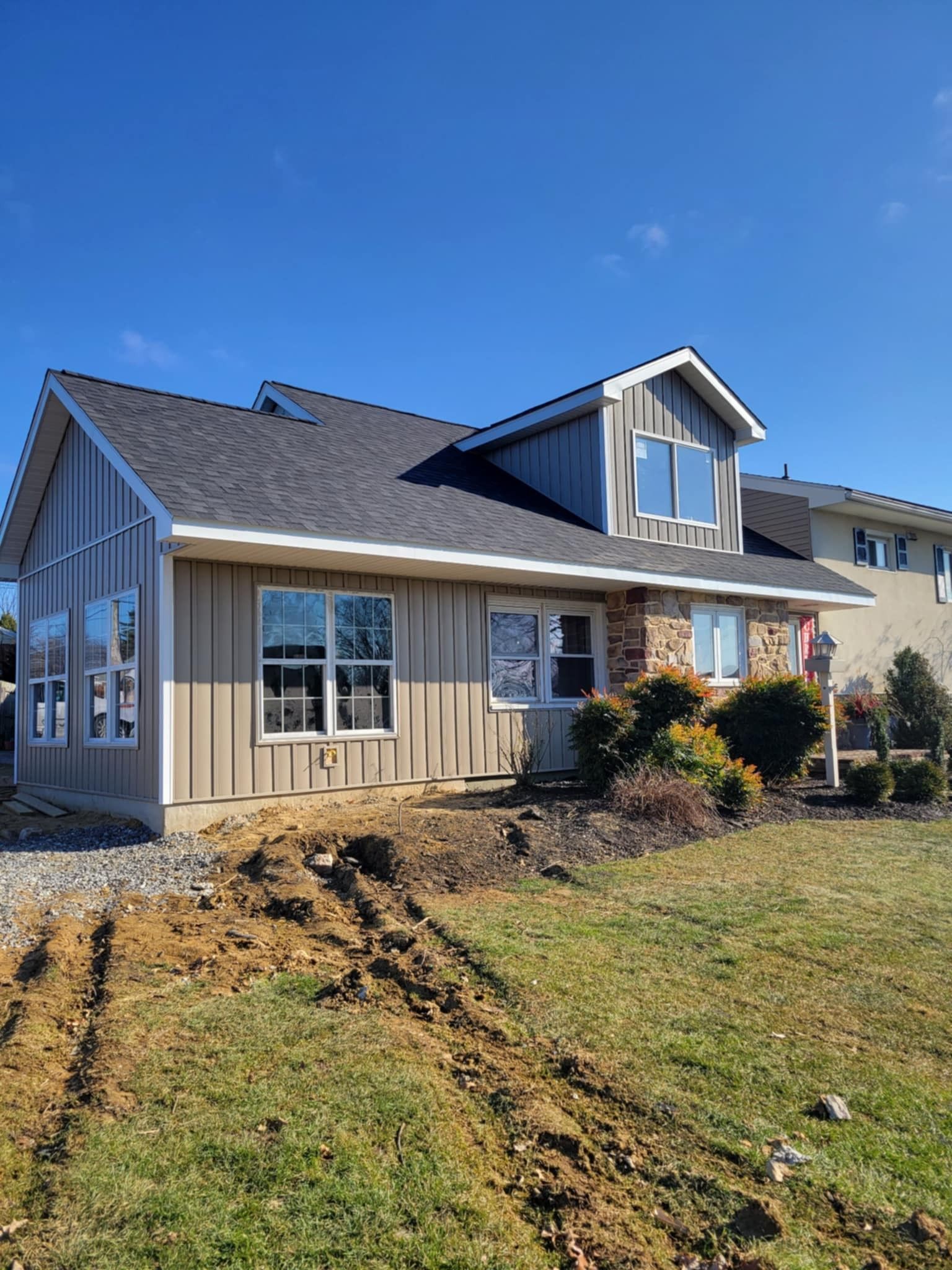 House with light brown siding, dark roof, and blue sky. A dirt path leads from the yard.