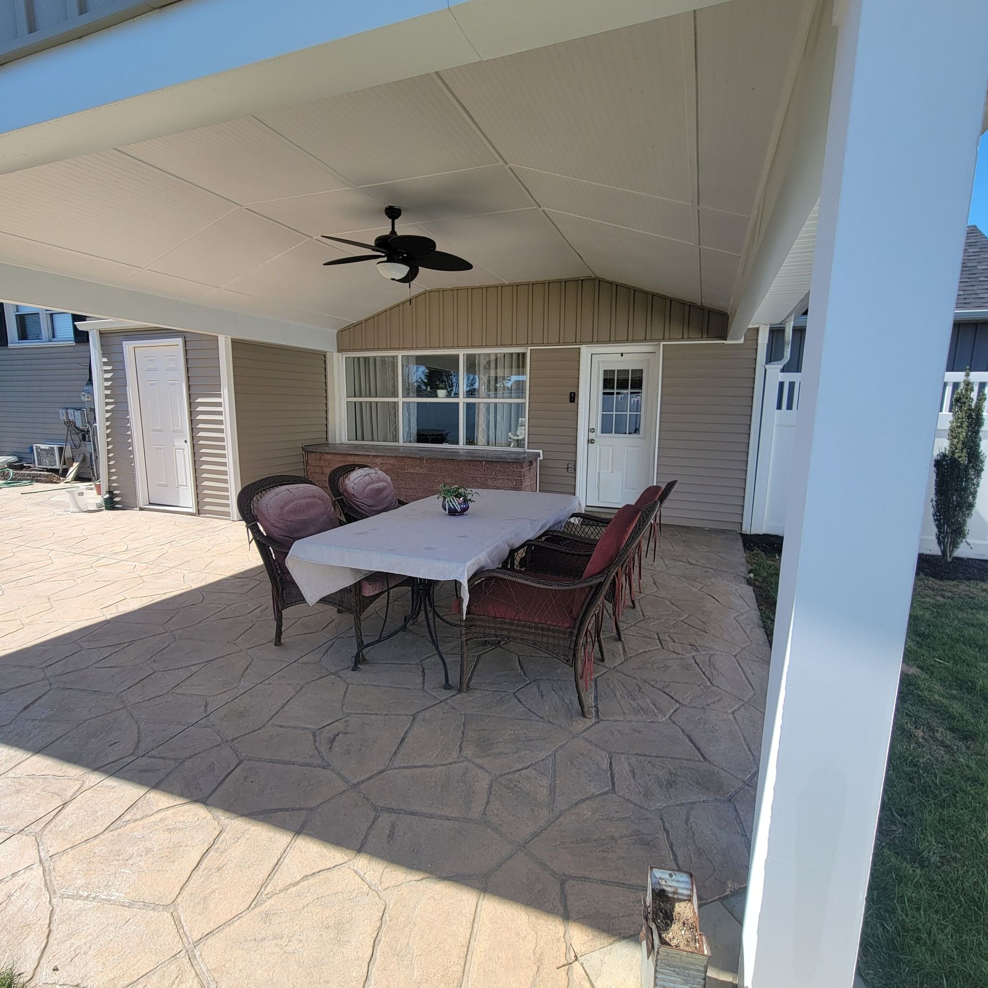 Covered patio with dining set, ceiling fan, and tan siding.