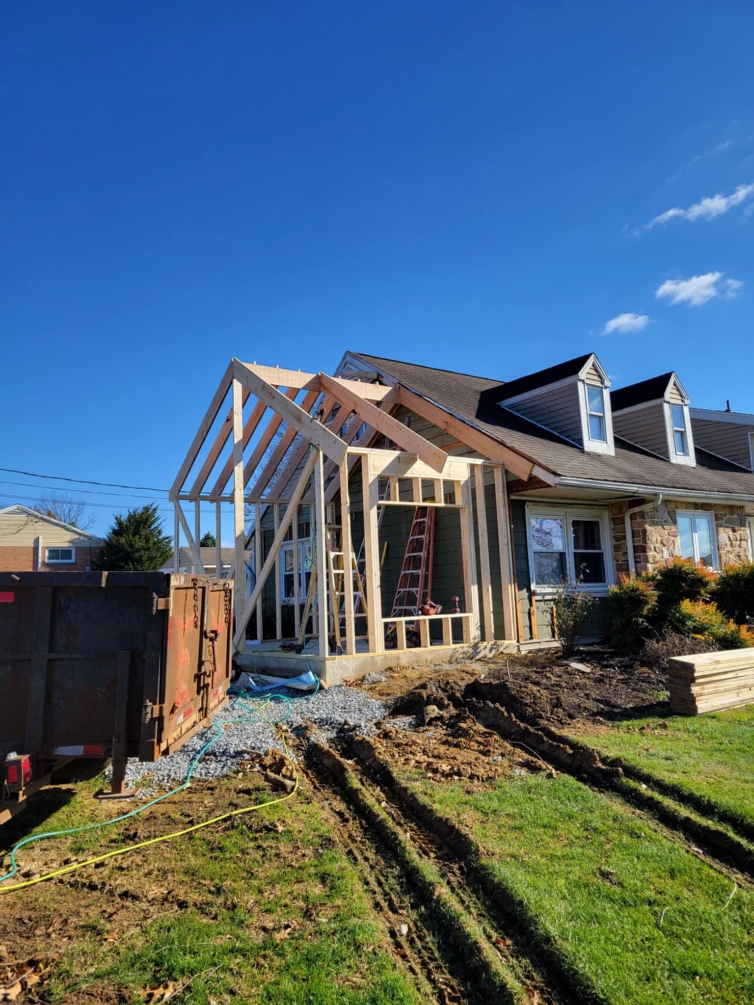 House undergoing construction; new frame being built onto existing structure, sunny day, blue sky.