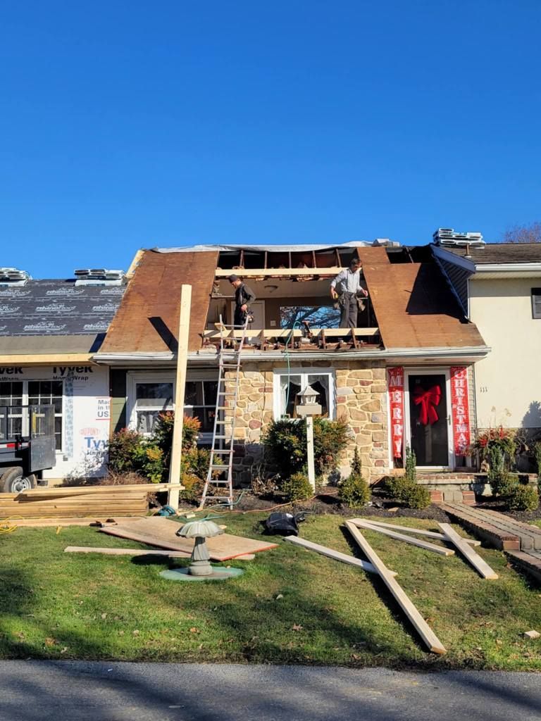 Home under construction: roof partially removed; workers, ladders, and building materials visible outdoors.