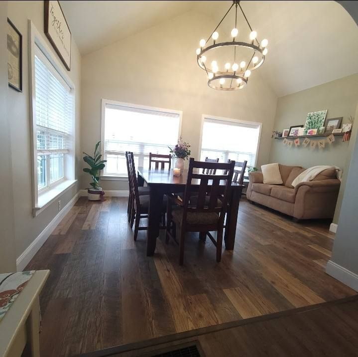Dining room with wood floors, a dark table, and a chandelier. A sofa is in the background.
