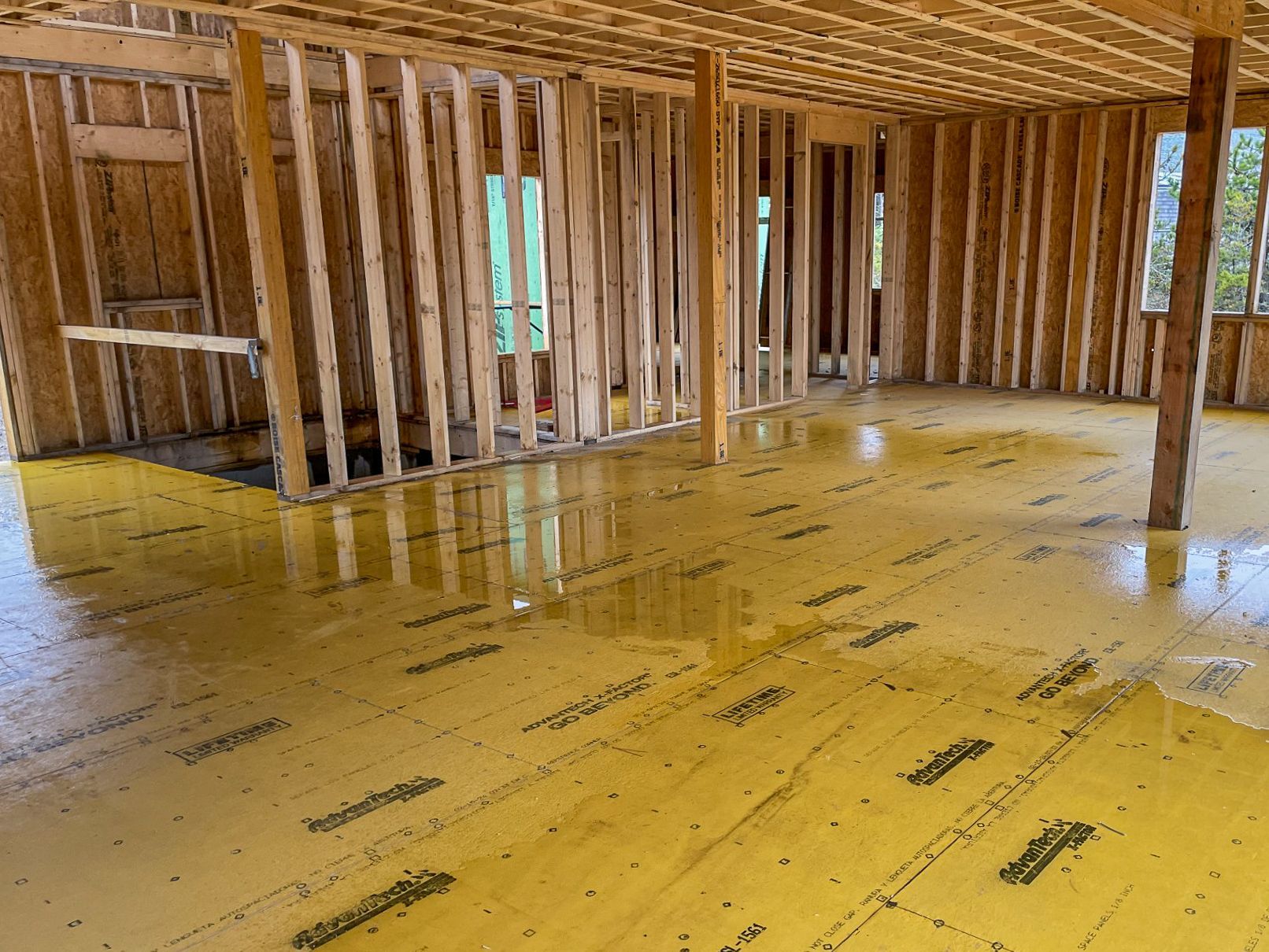 Interior of a house under construction with yellow flooring, wooden frames, and visible support beams.
